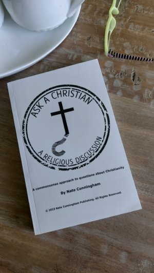 A copy of "Ask A Christian: A Religious Discussion" by Nate Cunningham lies on a wooden table, stamped with the Ask A Christian logo. Nearby are a pair of green-framed glasses with striped temples and a white ceramic bowl with eggs.